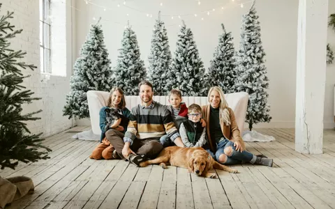 Family with a golden retriever on a sofa in front of snowy Christmas trees